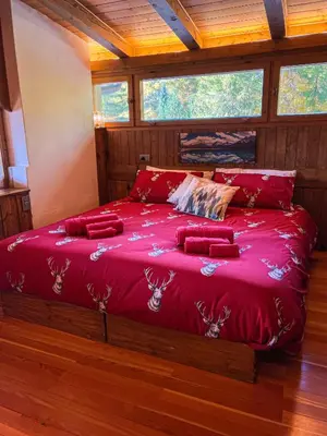 a bedroom with a bed with red sheets and two windows at Chalet vicino le piste da sci in Pocol