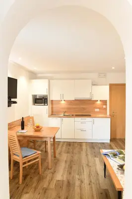 a kitchen with white cabinets and a wooden table and chairs at Haus Rosengarten in Tirolo