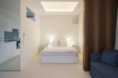 a white bedroom with a bed and a blue couch at Mirror Houses in Bolzano