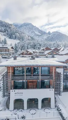 a building covered in snow with mountains in the background at Mölgg Dolomites Residence in San Vigilio Di Marebbe