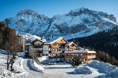 a building in the snow with mountains in the background at Hotel Ciurnadú in La Valle