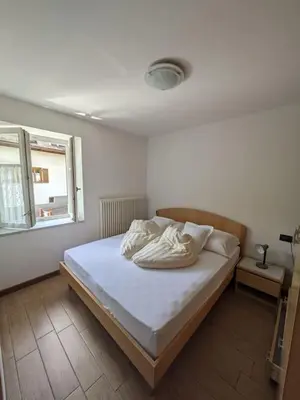 a bedroom with a bed with white sheets and a window at Comodità in centro a Tesero in Tesero