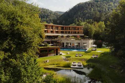 a building with a swimming pool next to a river at Taubers Bio Vitalhotel in Chienes