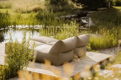 a couch sitting on a wooden deck near a pond at Taubers Bio Vitalhotel in Chienes