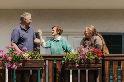 three people standing next to a fence with flowers at Pension Torr in San Martino in Badia