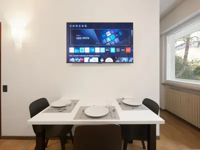 a white table with chairs and a tv on a wall at Central Palm Studio with free Parking in Merano