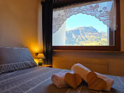 a bedroom with a large window with towels on a bed at Sogno sulle Dolomiti - Alpine Stay Apartments in Moena