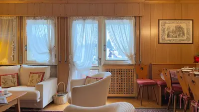 a living room with white chairs and a table and windows at Homeby, Casa Due Vette in Cortina dʼAmpezzo