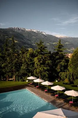 a swimming pool with umbrellas and tables and chairs at Design Hotel Tyrol in Rablà