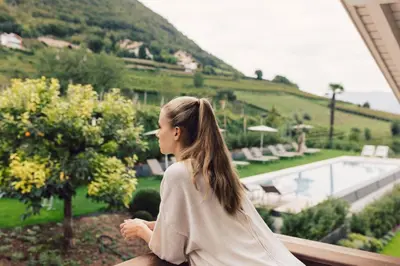 a woman sitting on a balcony looking out at a garden at Pomella's Guesthouse in Cortaccia