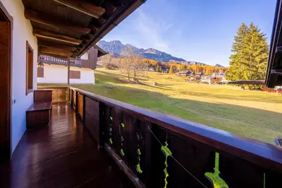 a balcony with a view of a field and mountains at GuestHost - Silent Peaks - Cortina's Wooden Haven in Cortina dʼAmpezzo
