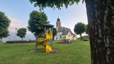 a playground with a slide in front of a church at Appartamento Casa AleF - L'affaccio sul Lagorai in Daiano