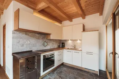 a kitchen with white cabinets and a wooden ceiling at Großkarnaiderhof Ferienwohnungen-Bauernhof-Dolomiten-Natur Pur in Luson