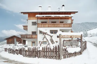 a building with a fence in the snow at Großkarnaiderhof Ferienwohnungen-Bauernhof-Dolomiten-Natur Pur in Luson