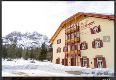 a building in the snow with mountains in the background at Chalet con vista villaggio ploner in Dobbiaco