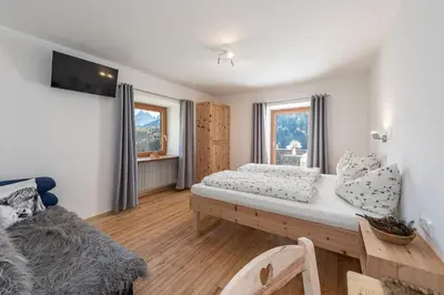 a bedroom with a bed and a couch and two windows at Austillerhof - Urlaub auf dem Bauernhof in Funes