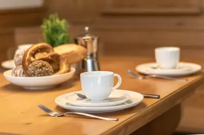 a table with cups and plates of food and bread at Apartment Rohrer - Zirm - Zirbe Cirmolo mit Schloss- und Schourtblick in Sarntal