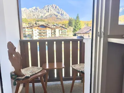 a balcony with a table and chairs and a mountain at Dolce Casa Cortina Centro-Ski in Cortina dʼAmpezzo