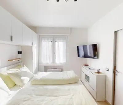 a white bedroom with a bed and a tv at Manzoni 99 in Merano