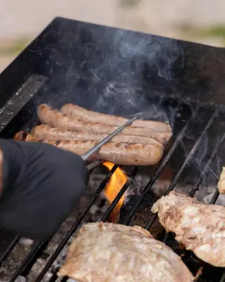 a person cooking sausages on a grill with a spatula at Chalet Al Maso Val Calamento in Telve