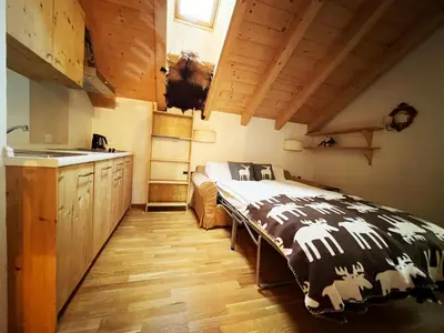 a bedroom with a bed and a kitchen with wooden ceilings at Lüch dl Mone y Chalets in Badia