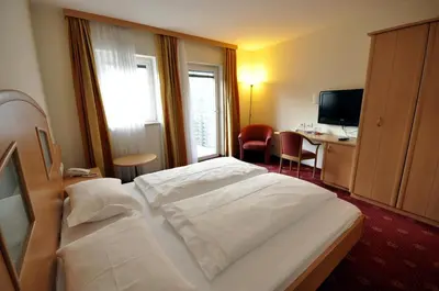 a hotel room with a white bed and a desk at Cityhotel Tallero in Bressanone