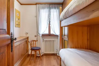 a bedroom with a bed and a chair and a window at Cozy 3 bedroom with access to garden in Cortina dʼAmpezzo