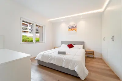 a white bedroom with a bed and a kitchen at Villa Silvio in Castello di Fiemme