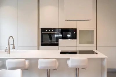 a kitchen with white cabinets and a counter with white stools at Villa Silvio in Castello di Fiemme