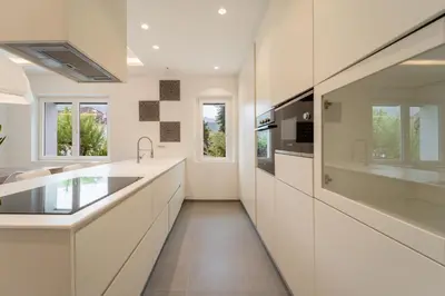 a kitchen with white counters and sinks and windows at Villa Silvio in Castello di Fiemme