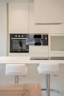 a kitchen with white cabinets and a counter with stools at Villa Silvio in Castello di Fiemme