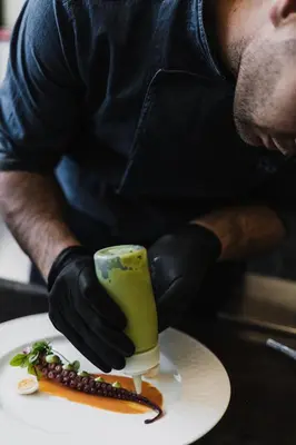 a man in black gloves preparing food on a plate at Hotel Mühlbacherhof in Lagundo