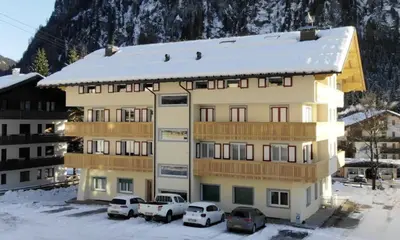 a building with cars parked in front of it in the snow at Cèsa Carlotta by AMA Val di Fassa in Campitello di Fassa