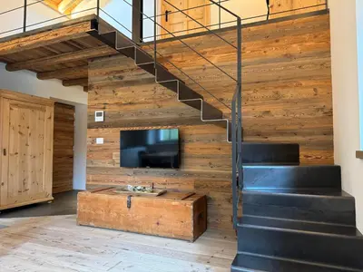 a living room with a staircase and a tv and a wooden wall at Alpen Chic in Cavalese