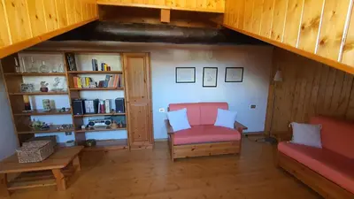 a living room with a red chair and a book shelf at Dolomites Holiday Home in Rivamonte