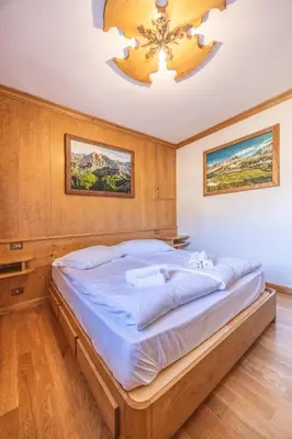 a large bed in a bedroom with a chandelier at Casa Ronco, tranquilla e confortevole in Cortina dʼAmpezzo