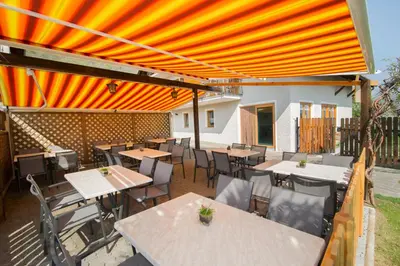 an outdoor patio with tables and chairs and an orange canopy at Garni Gartenheim in Caldaro