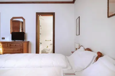 a white bedroom with a bed and a mirror at GuestHost - Cortina Heart Retreat with Parking in Cortina dʼAmpezzo