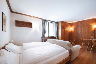 a bedroom with two white beds and a table at GuestHost - Cortina Heart Retreat with Parking in Cortina dʼAmpezzo
