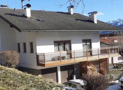 a white house with a deck and mountains in the background at casa elvira in Castello di Fiemme