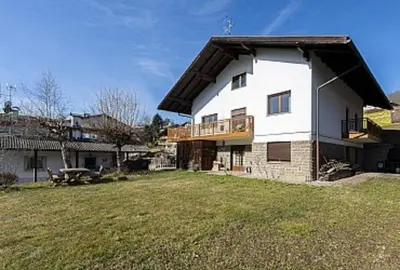 a large white house with a balcony and a yard at casa elvira in Castello di Fiemme