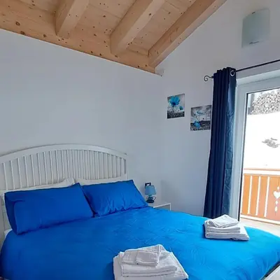 a bedroom with a blue bed and a window at Dream Apartments Moena in Moena