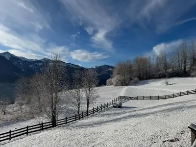 a fence in a snow covered field with trees and mountains at B&B Belvedere in Daiano
