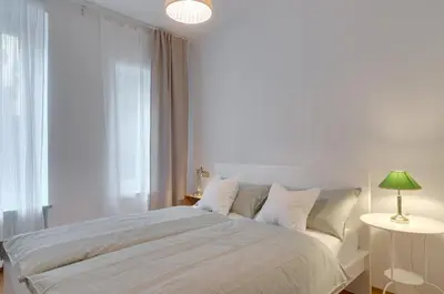 a white bedroom with a large bed with a green lamp at Frida's apartment in Merano