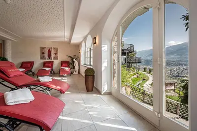 a room with red chairs and a balcony with a view at Hotel Restaurant Waldea in Marlengo