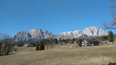 a large mountain range with a house in a field at Appartamento Croda in Cortina dʼAmpezzo