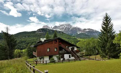 a barn in a field with mountains in the background at Appartamento Croda in Cortina dʼAmpezzo