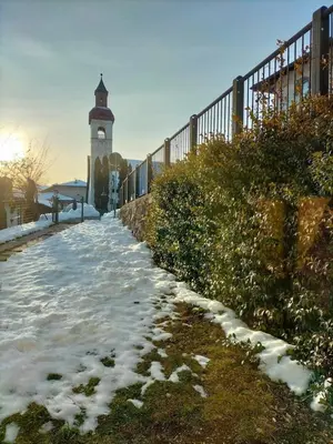 a snow covered path with a clock tower in the background at Apartment Rosanna Val di Non, Sanzeno in Sanzeno
