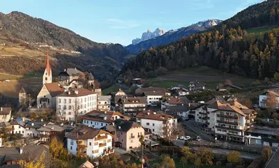 a town in the mountains with houses and a church at Der Unterwirt Guesthouse - Pool & JRE Restaurant in Chiusa