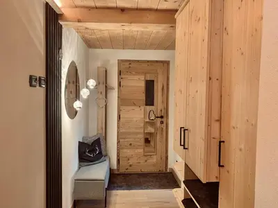 a hallway with a wooden door and a chair at Snowflake Apartment in Moena